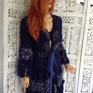 May include: A navy blue crochet cardigan with a beaded design and a blue ribbon tie. The cardigan has a long, flowing silhouette and a delicate lace trim.