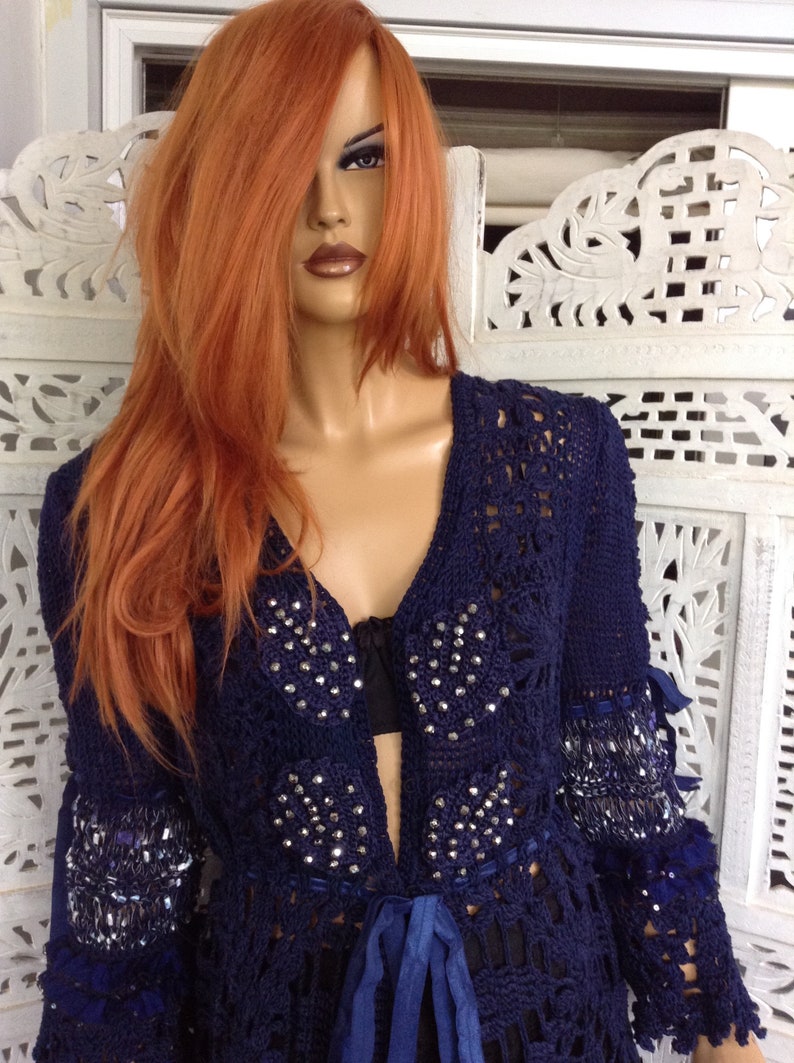 May include: A navy blue crocheted cardigan with a tie closure and embellished with rhinestones. The cardigan has long sleeves and a loose fit.