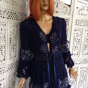 May include: A navy blue crocheted cardigan with a beaded design and a ribbon tie. The cardigan has a long, flowing silhouette and a delicate lace pattern.