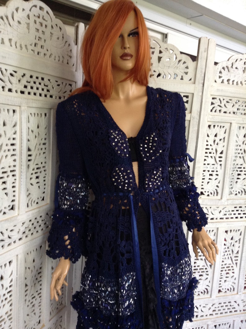 May include: A navy blue crocheted cardigan with a beaded design and a ribbon tie. The cardigan has a long, flowing silhouette and a delicate lace pattern.