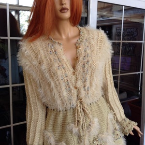 May include: A cream knitted cardigan with a fluffy texture and beaded embellishments. The cardigan has long sleeves, a V-neck, and a tie at the waist.