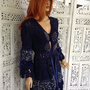 May include: A navy blue crochet cardigan with a long, open front and a lace trim. The cardigan is decorated with silver sequins and has a blue ribbon tie.