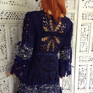 May include: A navy blue crochet dress with a lace back and beaded trim. The dress has long sleeves and a flowing skirt.