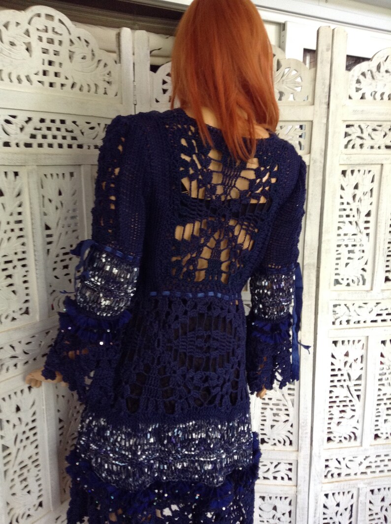 May include: A navy blue crochet dress with a lace back and beaded trim. The dress has long sleeves and a flowing skirt.