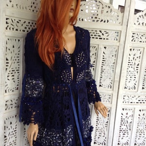May include: A navy blue crocheted cardigan with a lace pattern and beaded embellishments. The cardigan has a long, flowing silhouette and a tie at the waist.