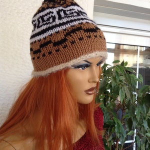 May include: A brown, black, and white knitted hat with a white fur trim. The hat has a geometric pattern and is worn by a mannequin with long, red hair.