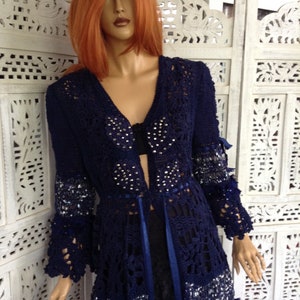 May include: A navy blue crocheted cardigan with a long, open front and long sleeves. The cardigan is embellished with silver sequins and rhinestones. It has a blue ribbon tie at the waist.
