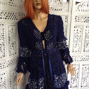 May include: A navy blue crocheted cardigan with a lace pattern and silver embellishments. The cardigan has a V-neckline and long sleeves with a ruffled trim.