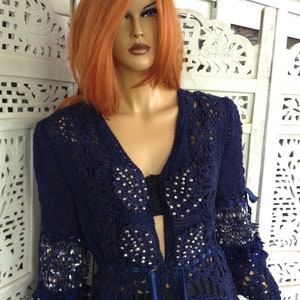 May include: A navy blue crocheted cardigan with a long, open front and beaded embellishments. The cardigan has a delicate, lacy pattern and a flowing silhouette.