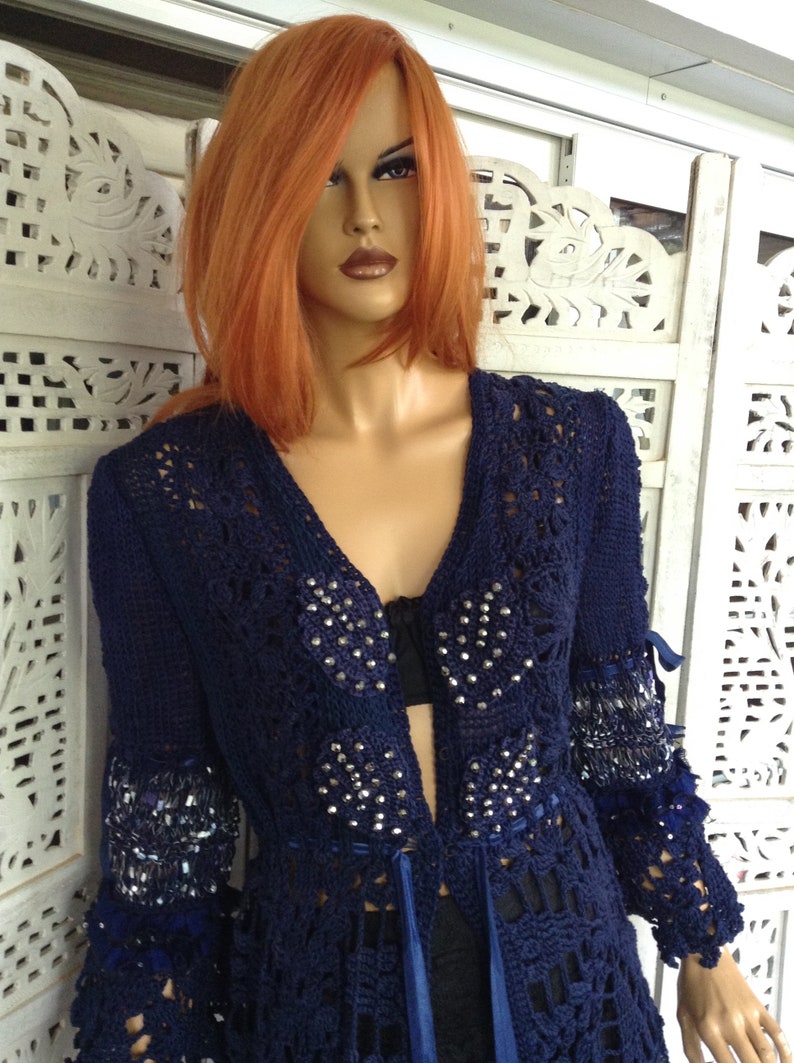May include: A navy blue crocheted cardigan with a long, open front and beaded embellishments. The cardigan has a delicate, lacy pattern and a flowing silhouette.