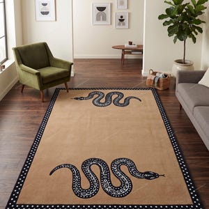 May include: A rectangular area rug featuring a tan centre field with two black snake illustrations, one smaller and one larger, oriented horizontally. The rug is framed by a wide black border decorated with a repeating pattern of white polka dots.