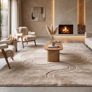 Op de afbeelding: Een groot rechthoekig vloerkleed in een neutrale beige tint met een verhoogd, gestructureerd slangachtig patroon dat over het oppervlak slingert. Het kleed is gemaakt met een pluche, hoogpolige textuur en ligt in een woonkamer met meubels.
