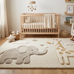 May include: A rectangular area rug featuring a textured, cream-coloured background with raised, plush appliques of a grey elephant and a tan and white giraffe. The rug includes small cloud and circle shapes, creating a soft, tactile surface design.