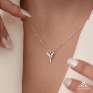 May include: A silver fairy pendant necklace with crystal embellishments. The pendant depicts a fairy with detailed wings, suspended from a delicate chain. The necklace is shown against a neutral backdrop, emphasizing the intricate design and sparkle of the jewellery.