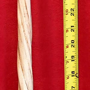 May include: A light-colored, carved wooden wand with a spiral design, approximately 35 inches long, is displayed against a red background. A yellow measuring tape is positioned next to the wand for scale.