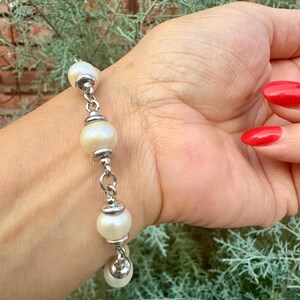 May include: A bracelet featuring white, round, lustrous pearls alternating with polished silver-toned metal beads. The pearls are connected by silver-toned metal links, creating a structured chain design that wraps around the wrist.