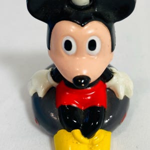 May include: A molded plastic figurine of Mickey Mouse sitting inside a black circular inner tube. The character has a black head with large ears, a peach-colored face, white gloves, red shorts, and yellow shoes. A small white light socket is on top.