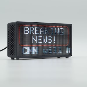 Peut inclure: Un appareil d'affichage num&eacute;rique LED noir rectangulaire avec un panneau lat&eacute;ral &agrave; motif en nid d'abeille. L'&eacute;cran affiche le texte BREAKING NEWS! en lettres blanches dans un cadre rectangulaire rouge, avec le texte partiel CHN will h en dessous.