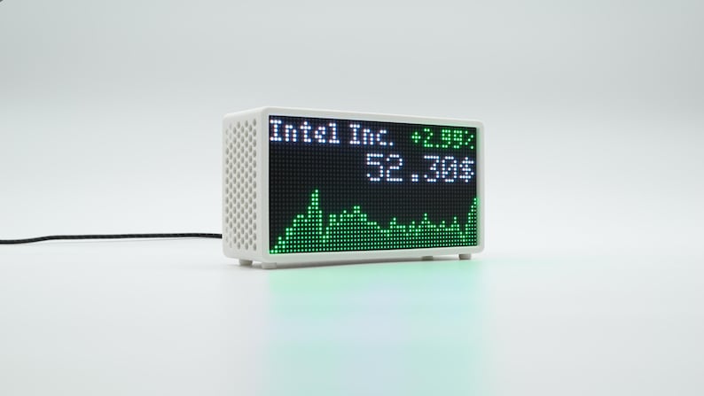 Peut inclure: Un appareil d'affichage num&eacute;rique blanc rectangulaire avec un panneau lat&eacute;ral perfor&eacute;. L'&eacute;cran affiche le texte Intel Inc., la valeur 52.30$, un pourcentage de +2.99% et un graphique lin&eacute;aire vert repr&eacute;sentant des donn&eacute;es boursi&egrave;res. Un fin c&acirc;ble noir est attach&eacute;.