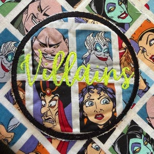 May include: A fabric panel featuring a repeating grid of various animated villain characters in colorful squares. A circular black embroidered patch is centered over the grid, displaying the word Villains in bright lime green cursive thread.