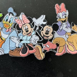 Pode incluir: Um emblema de tecido bordado apresentando um grupo de seis personagens de desenho animado, incluindo Pateta, Pato Donald, Minnie Mouse, Mickey Mouse, Margarida e Pluto. Os personagens estão dispostos lado a lado em um design colorido e detalhado.