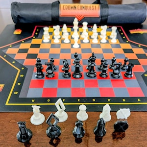 May include: A chess set with black and white pieces arranged on a black, red, and orange checkered board. The board has the text "CROWN CONQUEST" on it. A black carrying case with the same text is behind the board.