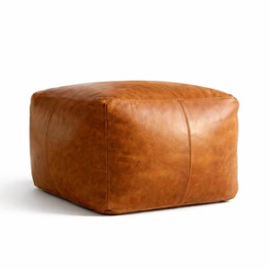 May include: A square, brown leather ottoman. The ottoman is a warm, medium brown color with visible stitching on the corners and sides. The leather has a slightly distressed appearance.