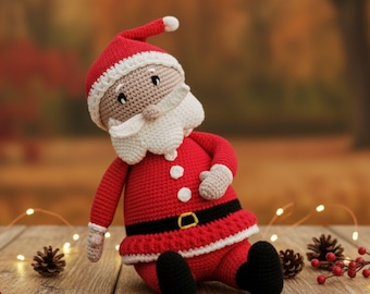 May include: A handmade crochet Santa Claus doll. The doll is primarily red with white trim on the hat and beard. It has black boots, a black belt with a gold buckle, and beige gloves. The doll is sitting on a wooden surface.