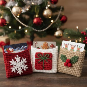 May include: Three crocheted gift card holders in red, white, and tan, with Christmas-themed designs. The red holder features a white snowflake, the white holder has a red gift, and the tan holder displays holly and berries. Cards with festive images are visible.