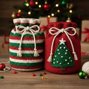 Może przedstawiać: Dwa szydełkowe worki na prezenty świąteczne. Jeden jest w czerwono-zielono-białe paski, a drugi jest czerwony z zieloną aplikacją choinki. Oba mają białe zamknięcia ze sznurkiem i frędzlami. Worki leżą na drewnianej powierzchni.