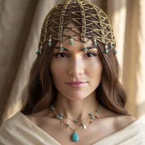 May include: A gold-toned crocheted headpiece featuring a lattice pattern adorned with small white pearls and light blue turquoise-colored stones along the edge, paired with a matching two-layer gold chain necklace with a teardrop turquoise pendant.