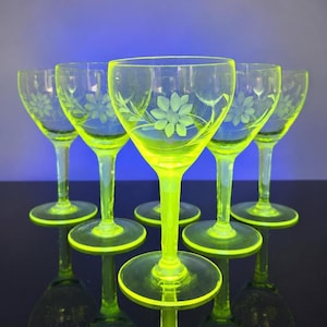 Può includere: Un set di cinque calici giallo-verde neon, ognuno caratterizzato da un delicato motivo floreale inciso sulla coppa. I bicchieri presentano una finitura liscia e traslucida e sono disposti in gruppo, brillando di una tonalità vivace e luminosa.