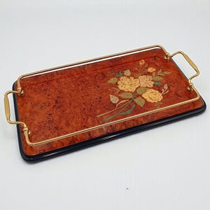 Könnte beinhalten: Rechteckiges Serviertablett mit Maserholz-Finish und goldfarbenen Griffen. Das Tablett hat ein Blumendesign mit gelben und grünen Akzenten. Das Tablett hat einen schwarzen Rand.