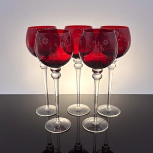 Peut inclure: Ensemble de six verres à vin rouges avec des pieds et des bases transparents. Chaque verre présente un motif floral gravé sur le bol. Les verres sont disposés en rangée, se reflétant sur une surface sombre.