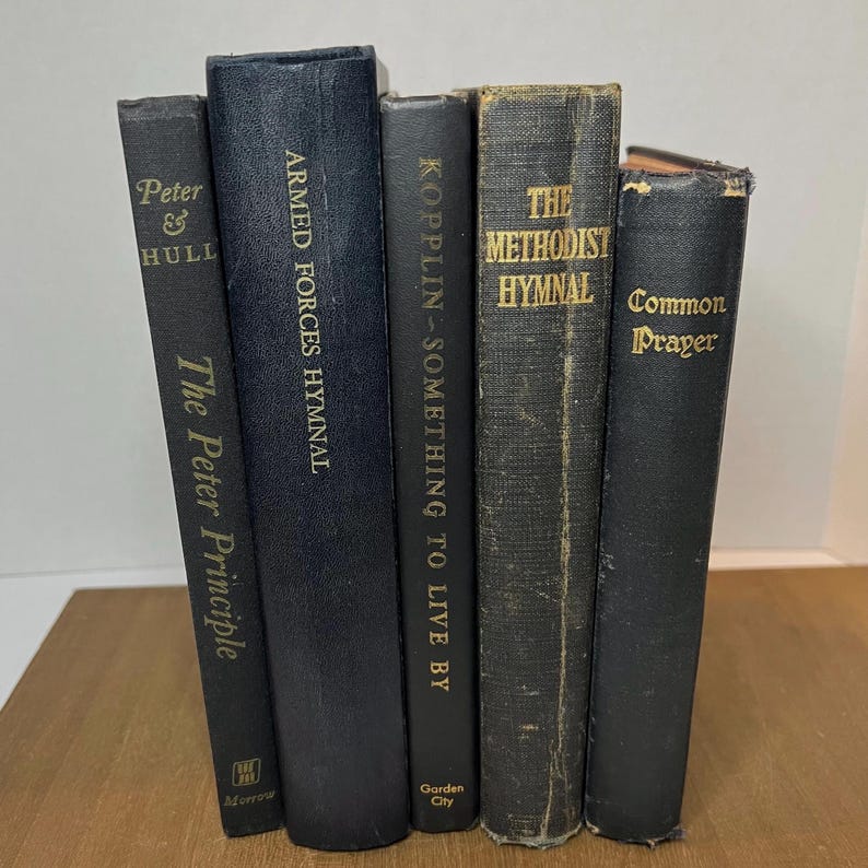 May include: Five antique books with dark covers are displayed. The titles include "The Peter Principle," "Armed Forces Hymnal," "Kopplin - Something to Live By," "The Methodist Hymnal," and "Common Prayer." The text is in gold lettering.