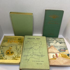 May include: A collection of vintage books with green covers. Titles include "Stories From Japan", "Forgotten Trails", and "El Mundo Es Ancho Y Ajeno". The books are arranged on a light surface, showcasing their aged appearance and historical significance.