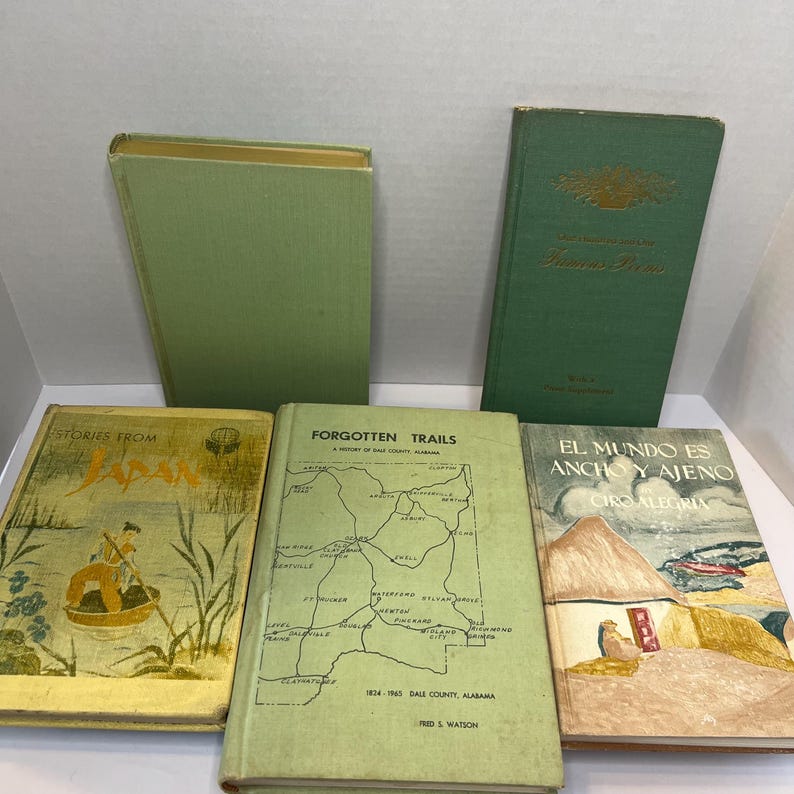 May include: A collection of vintage books with green covers. Titles include "Stories From Japan", "Forgotten Trails", and "El Mundo Es Ancho Y Ajeno". The books are arranged on a light surface, showcasing their aged appearance and historical significance.