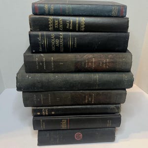 May include: A collection of vintage books with dark covers, including titles like "Nicholas and Alexandra" and "The Chain." The books are stacked, showing signs of age and wear, with varying sizes and colours.