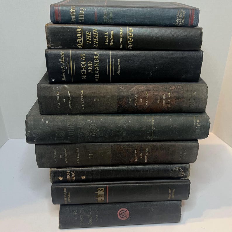 May include: A collection of vintage books with dark covers, including titles like "Nicholas and Alexandra" and "The Chain." The books are stacked, showing signs of age and wear, with varying sizes and colours.