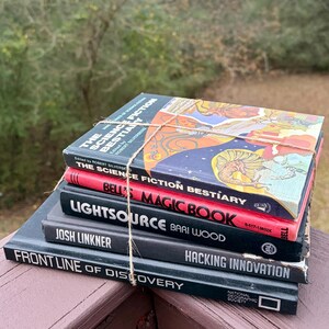 May include: A collection of vintage books bound with string. Titles visible include "The Science Fiction Bestiary" and "Bell's Magic Book". The books feature colourful covers and are stacked on a wooden surface, evoking a sense of nostalgia.