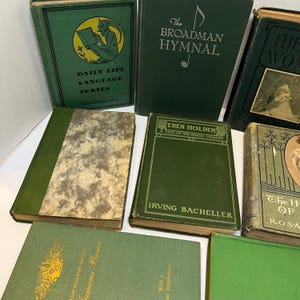 May include: A collection of vintage books with green covers. Titles include "Daily Life Language Series," "The Broadman Hymnal," and "Eben Holden." The books vary in size and design, with some featuring gold lettering and illustrations.