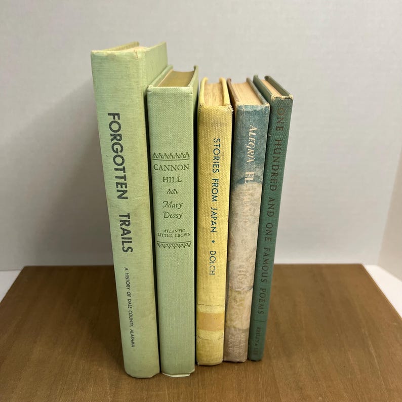 May include: A collection of vintage books with various titles and colors. The spines are in shades of green, yellow, and blue. Titles include "Forgotten Trails," "Cannon Hill," "Stories From Japan," "Alegria El," and "One Hundred and One Famous Poems."