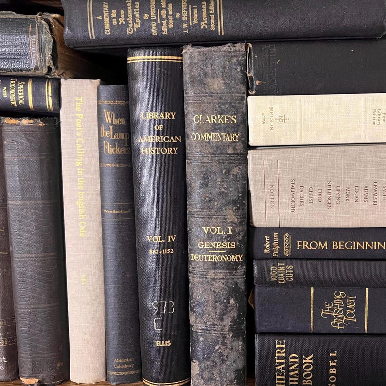 May include: A selection of vintage books with dark-coloured spines. Titles visible include "Library of American History," "Clarke's Commentary," and "The Poet's Calling in the English Ode." The books are arranged on a shelf.