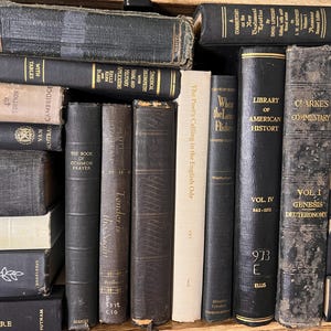 May include: A selection of vintage books in various sizes and colours. The spines are mostly dark, with gold lettering and signs of age. The books are stacked and arranged, giving the impression of a library or a collection of old books.