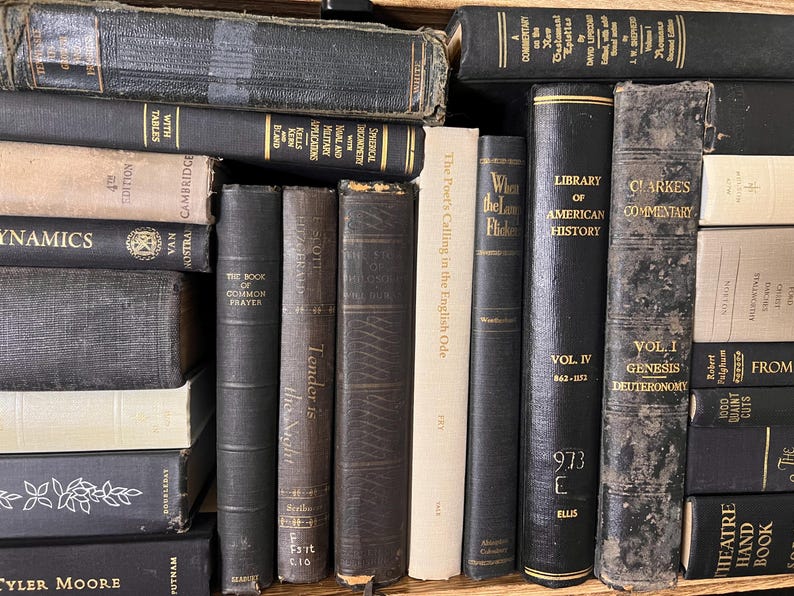 May include: A selection of vintage books in various sizes and colours. The spines are mostly dark, with gold lettering and signs of age. The books are stacked and arranged, giving the impression of a library or a collection of old books.