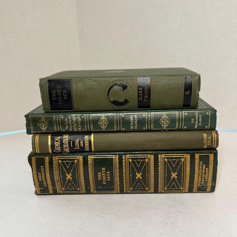 May include: A stack of four vintage books with green and gold covers. Titles include "The Gilded Age," "The Forsyte Saga," and "Chemical Calculations." The books are arranged in a neat pile, showcasing classic literature.