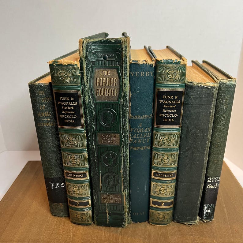 May include: A collection of antique books with dark green and blue covers. Titles include "The Popular Educator," "Funk & Wagnalls Standard Reference Encyclopedia," and "A Woman Called Fancy." The books are arranged in a semi-circle.