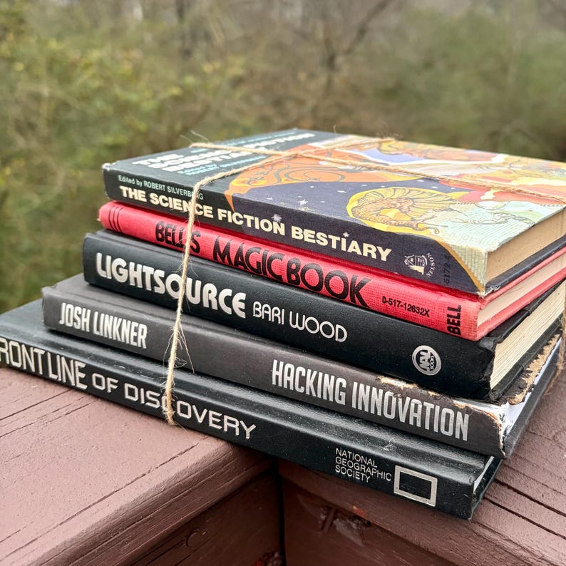 May include: A pile of old books bound with string. Titles visible are "The Science Fiction Bestiary", "Bells Magic Book", "Lightsource", "Frontline of Discovery", and "Hacking Innovation". The books are in various colours, including red, black, and blue.