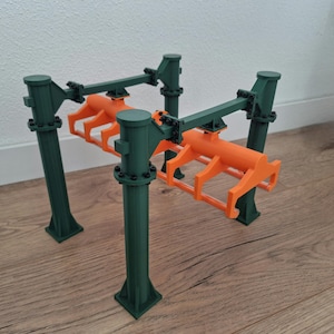 May include: A 3D-printed model featuring a green and orange color scheme. The structure has four green vertical supports with orange horizontal components. The design appears to be a mechanical or industrial model, possibly a crane or lifting mechanism.