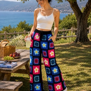 May include: Crochet pants featuring a vibrant granny square pattern with alternating black, blue, pink, and white floral motifs. These wide-leg trousers include a black drawstring waistband and a loose, comfortable fit, crafted from colorful yarn.